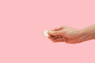 Hand holding a condom for safe sex, preventing pregnancy and sexually transmitted diseases on pink...