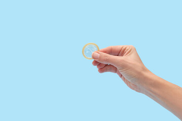 Hand holding a condom for safe sex and preventing pregnancy on blue background