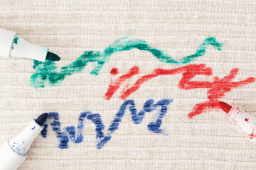 Brightly colored marker scribbles in green, red, and blue are spread across a light textured...