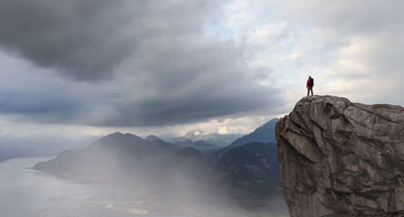 Adventurer Standing Atop a Steep Cliff Under Stormy Skies in Mountainous Terrain