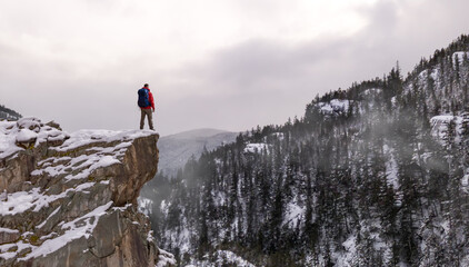 Man with Backpack Standing on Snowy Cliff Overlooking Winter Forest