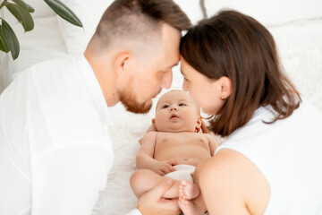 mom, dad with a baby, an international family, a Caucasian mom with an Asian husband and a baby in her arms in the bedroom gently hugs the baby holding in her arms, a place for text