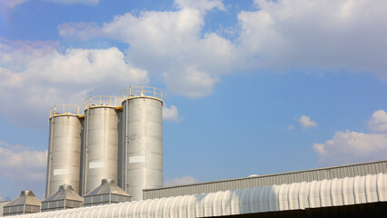 Stainless steel silo amidst blue sky. Warehouse for storing goods and maintaining product quality. Exterior of industrial factory with sky and clouds as background.