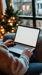 Laptop usage by a window, a decorated tree with string lights are in the background