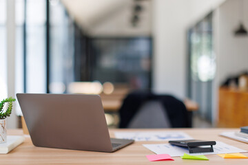 Laptop Computer, notebook, and eyeglasses sitting on a desk in a large open plan office space after working hours	