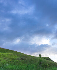 Hillside covered in green grass and a cloudy sky