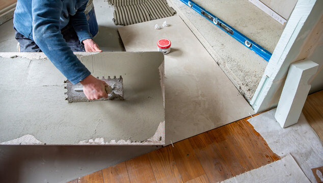 Focus sur la pose de carrelage. Mise en avant d'un homme qui &eacute;tale la colle sur le carrelage afin de le coller au sol. Gros plan sur l'encollage des carreaux de carrelage.