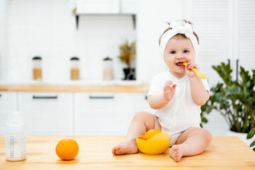 the baby eats on his own with a spoon in the kitchen at home, the concept of baby food, the child eats fruits oranges