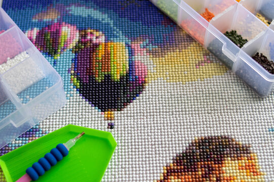 Close-up of a diamond painting and the tools needed to assemble it. Art therapy concept.