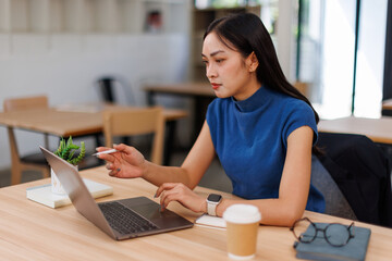 Asian professional business woman office worker analyst sitting at desk working on laptop thinking...
