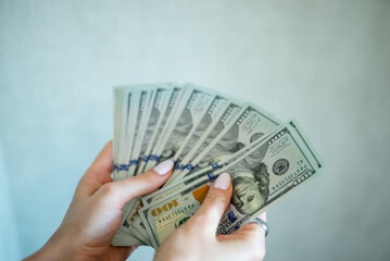 Counting cash in hands with hundred dollar bills in a modern indoor setting under natural light