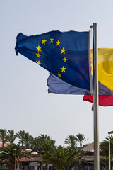 A flag of the European Union featuring twelve golden stars arranged in a circle against a blue background waving in the wind, a symbol of unity, solidarity, and harmony among the peoples of Europe