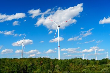 Fototapeta premium A stunning landscape featuring a row of large, modern wind turbines set against a clear blue sky with fluffy white clouds. These turbines symbolize clean energy and sustainability.
