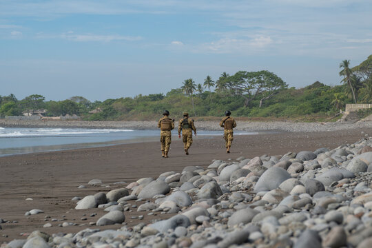 Armed national guards army personnel in camouflage uniform patrolling the beach area in a tourist town. La Libertad, El Salvador. 