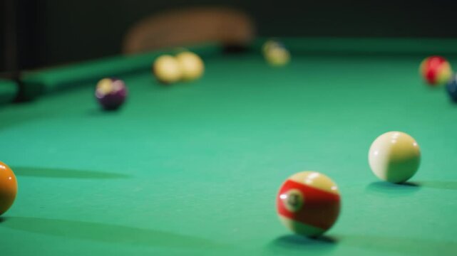 Close-up of cue stick striking white billiard ball, sending it toward orange ball on green pool table. Vibrant billiard balls scattered across surface capture intensity, precision, and movement