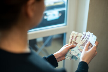 Counting cash in a well-lit room by a window, with emphasis on different banknotes and hand gestures, Ukrainian hryvnia