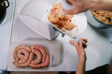 Cook stuffs the gut with minced meat on an electric meat grinder, pushing it with a pusher. Top view
