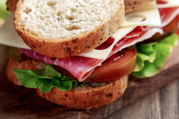 Cheese ham sandwich with tomatoes and lettuce on vintage cutting board. Whole wheat bread base. Fast food product