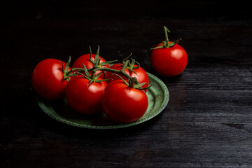 Top view of tomatoes on green plate on dark table, horizontal with copy space