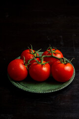 Top view of wet tomatoes on green plate on dark table, vertical with copy space