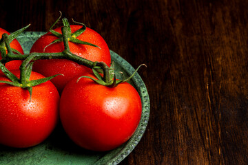 Close-up of tomatoes on green plate on wooden table, horizontal with copy space