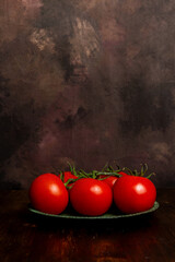 View of a group of tomatoes on a green plate on a table and a dark background, vertical with copy space