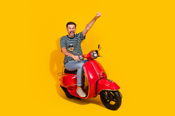 Energetic and cheerful young man riding a red scooter on a vibrant yellow background, expressing...