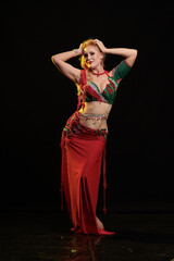 Young woman belly dancer in a red oriental costume on a black background