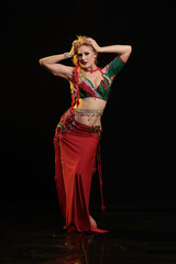 Young woman belly dancer in a red oriental costume on a black background
