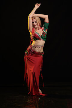 Young woman belly dancer in a red oriental costume on a black background