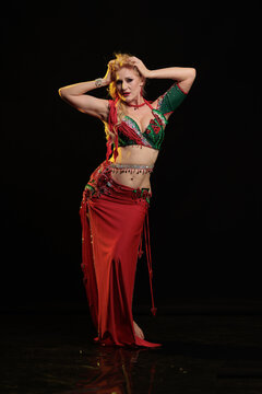 Young woman belly dancer in a red oriental costume on a black background