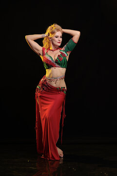 Young woman belly dancer in a red oriental costume on a black background
