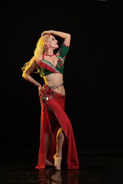 Young woman belly dancer in a red oriental costume on a black background