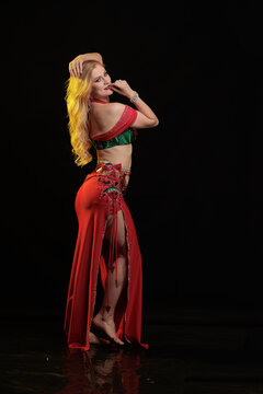 Young woman belly dancer in a red oriental costume on a black background