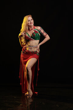 Young woman belly dancer in a red oriental costume on a black background