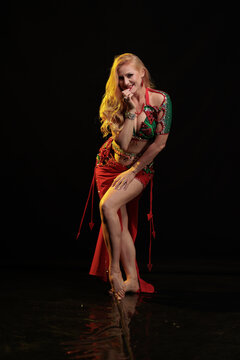 Young woman belly dancer in a red oriental costume on a black background