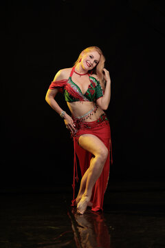 Young woman belly dancer in a red oriental costume on a black background