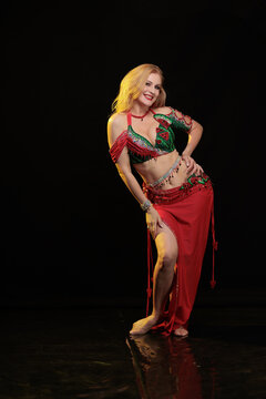 Young woman belly dancer in a red oriental costume on a black background