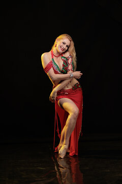 Young woman belly dancer in a red oriental costume on a black background