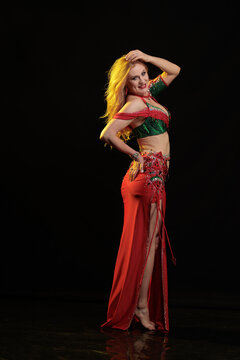 Young woman belly dancer in a red oriental costume on a black background