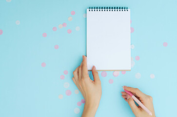 Well-groomed female hands with a pen near a notebook on a blue background. To-do list. Notes. Blank sheet for text.