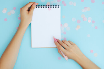 Well-groomed female hands with a pen near a notebook on a blue background. To-do list. Notes. Blank sheet for text.