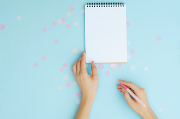 Well-groomed female hands with a pen near a notebook on a blue background. To-do list. Notes. Blank sheet for text.
