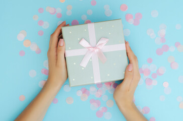 Well-groomed female hands hold a gift on a blue background. Festive background. Surprise.