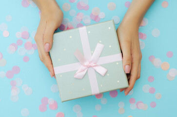 Well-groomed female hands hold a gift on a blue background. Festive background. Surprise.