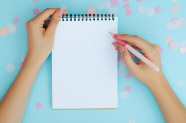 Well-groomed female hands with a pen near a notebook on a blue background. To-do list. Notes. Blank sheet for text.