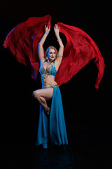 Young woman belly dancer in a blue oriental costume on a black background