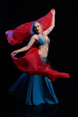 Woman in a blue costume oriental dancer posing and dancing on a black background