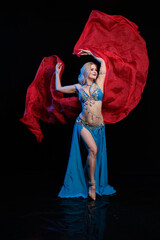 Fototapeta premium Woman in a blue costume oriental dancer posing and dancing on a black background