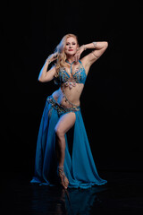 Obraz premium Woman in a blue costume oriental dancer posing and dancing on a black background